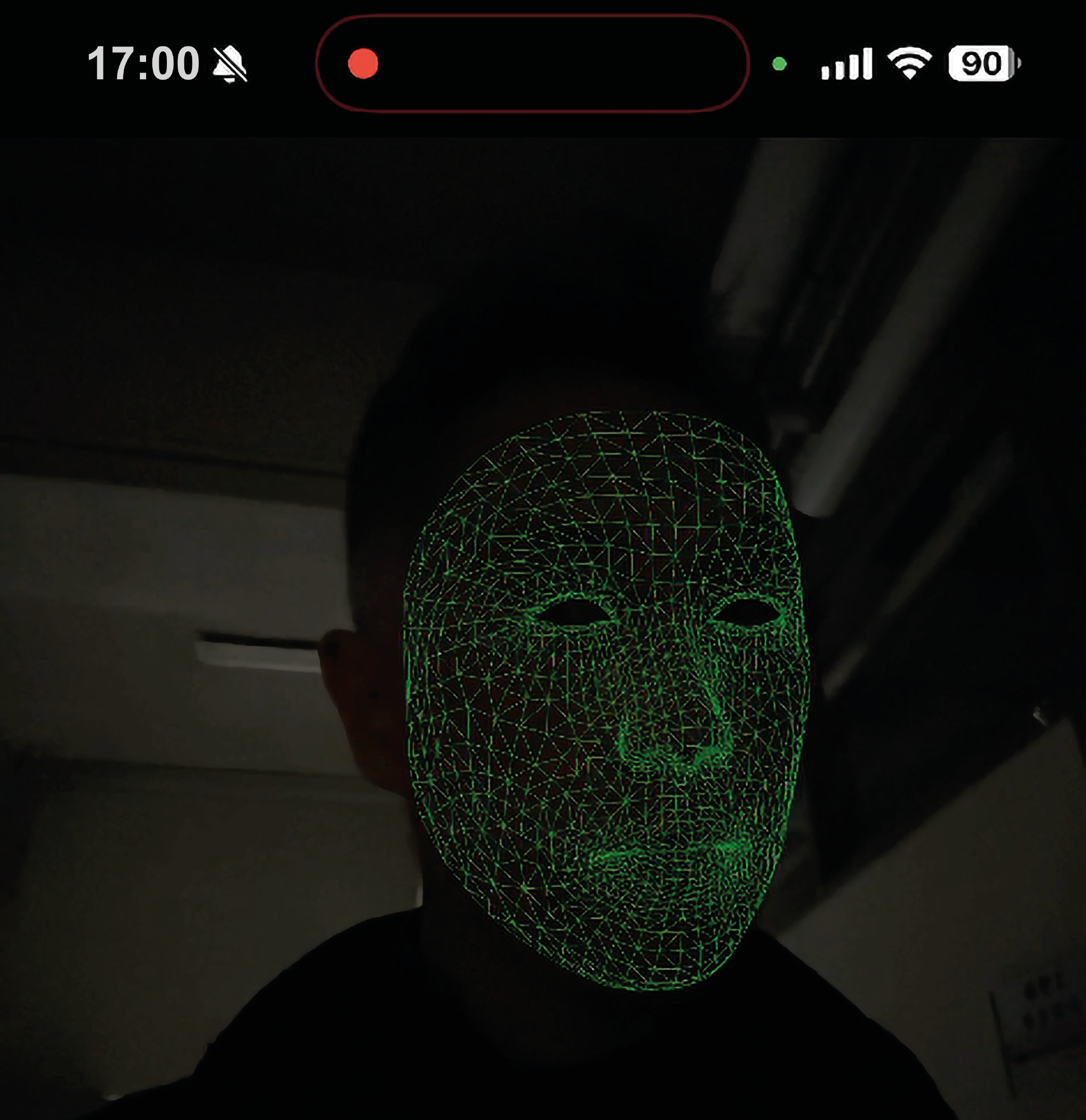 A green mesh is mapping a person's face. On the top of the picture you see some phone UI-symbols such as the battery icon, or the time. A red dot is indicating that the camera is on.