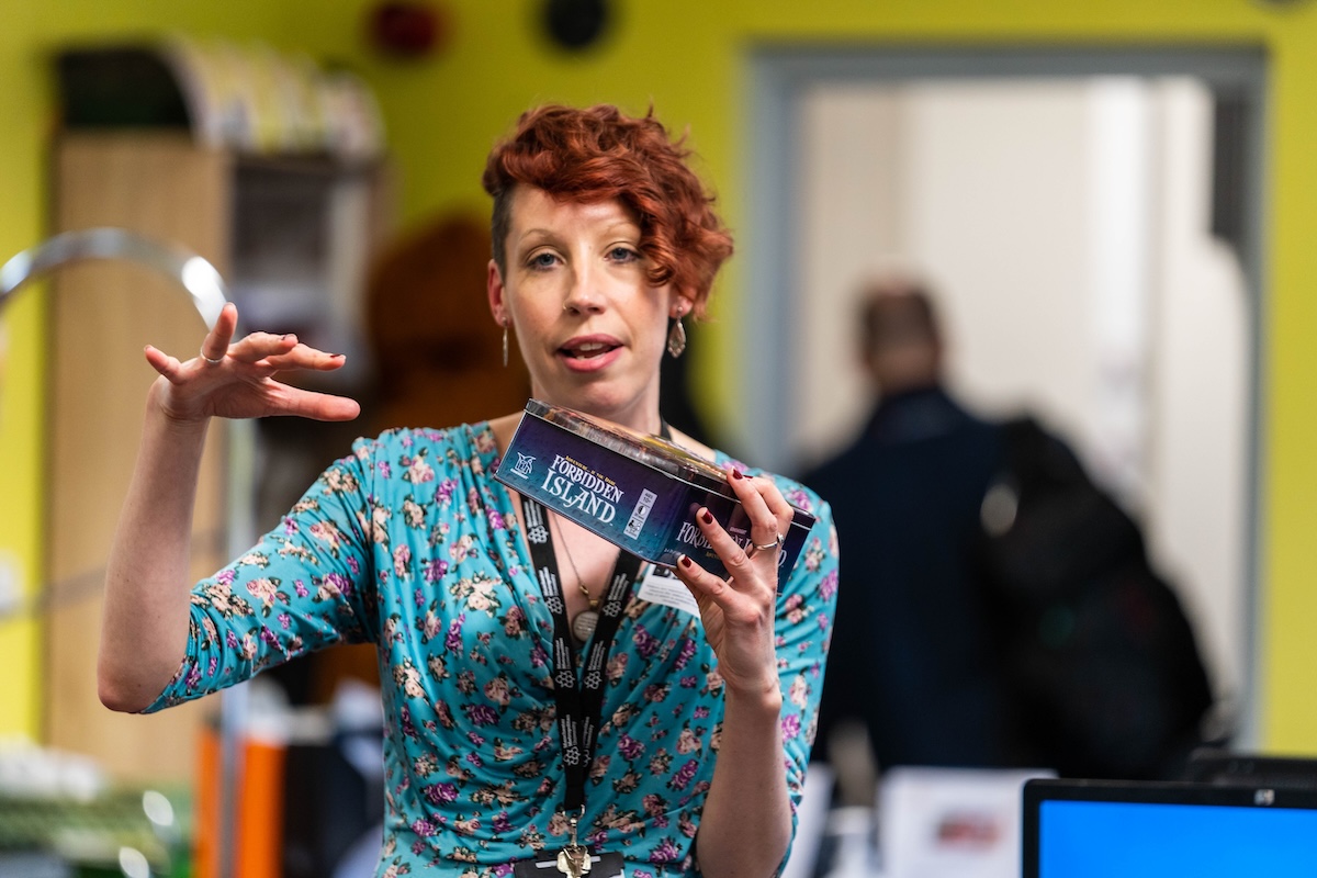 Dr. Chloé Wake (née Germaine) is holding the board game "Forbidden Island" in her hand. 