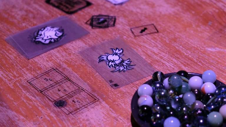 Candytrail is a board game that consists of see-through cards that each either form a path or have candies or candy-wrappers on them. You also get some marbles. Here you see the game set up as a close up in a purple tinted light. 