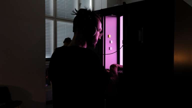 A tall man playing llami, which is illuminating his face in a pink light.